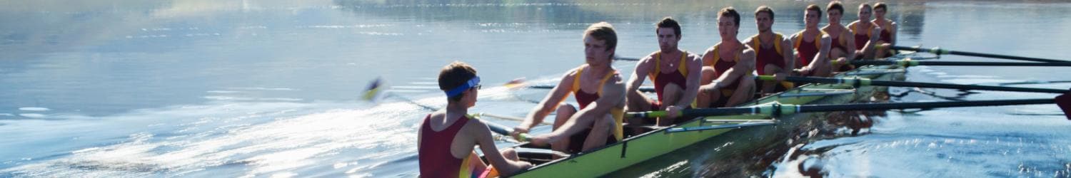 Ein Team aus acht Ruderern mit Steuermann steuert in passenden Uniformen ein Ruderboot über ruhiges Wasser.